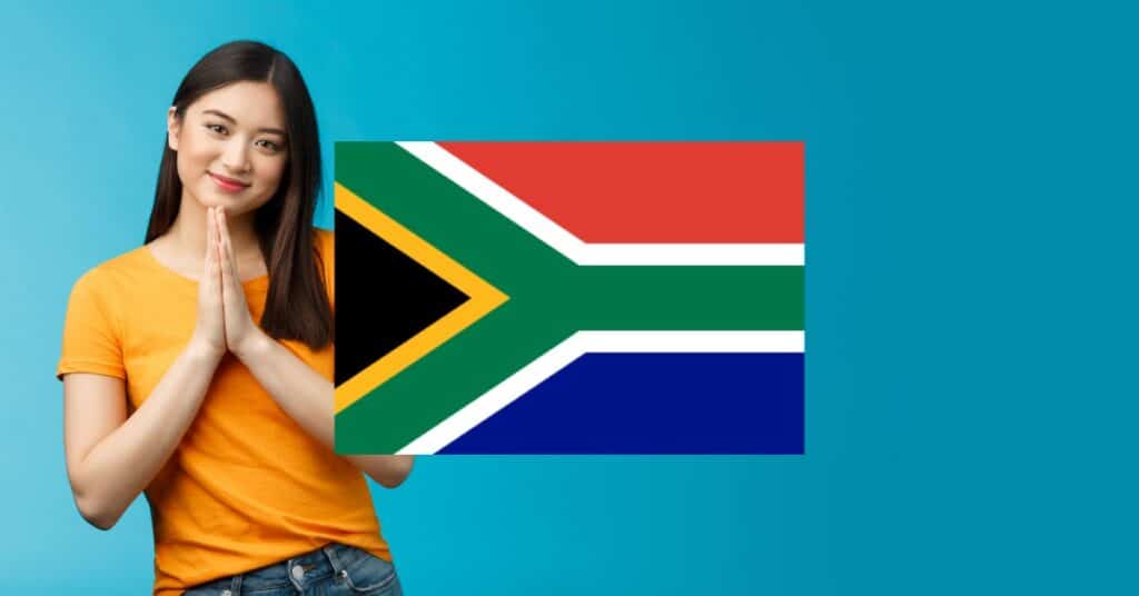 Woman greeting with hands held together against sky blue background and South Africa flag.